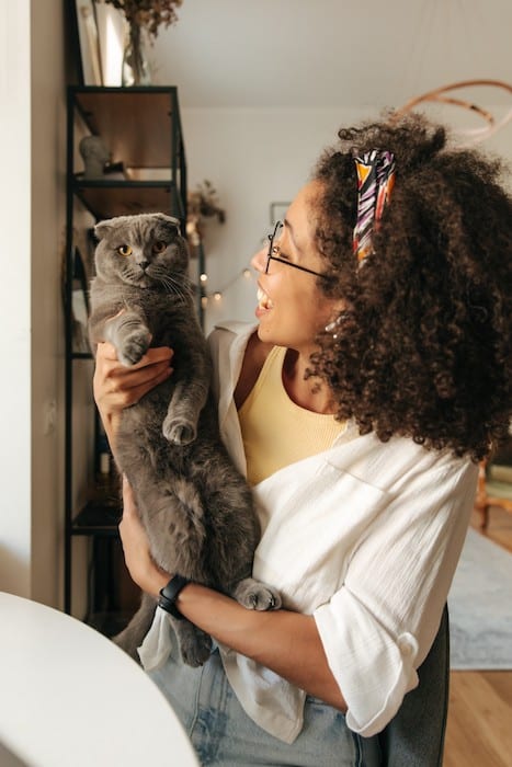 Une femme souriante en train de porter un chat gris